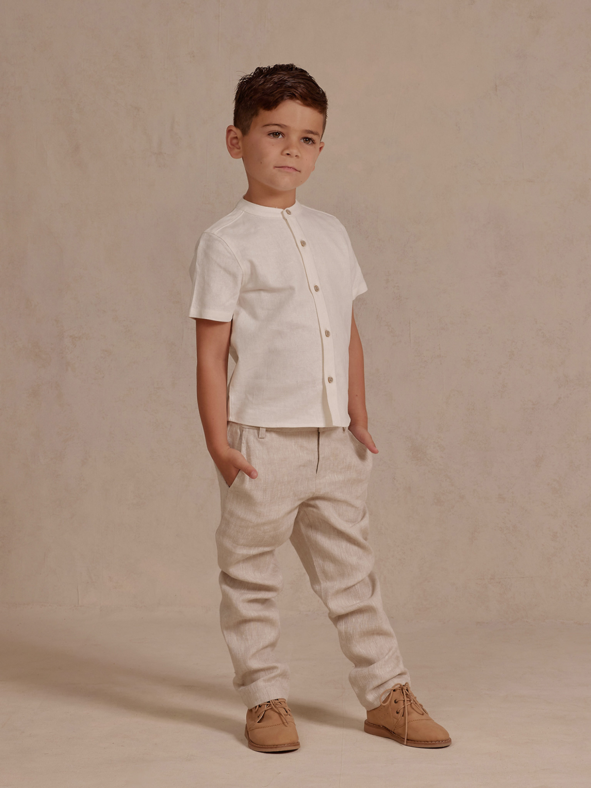 Child in a stylish light outfit with a short-sleeve shirt and beige pants, standing confidently against a neutral backdrop.