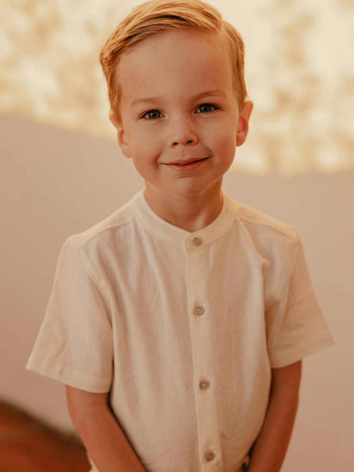 Smiling young boy in a light button-up shirt against a soft, neutral background.