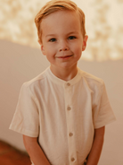 Smiling young boy in a light button-up shirt against a soft, neutral background.
