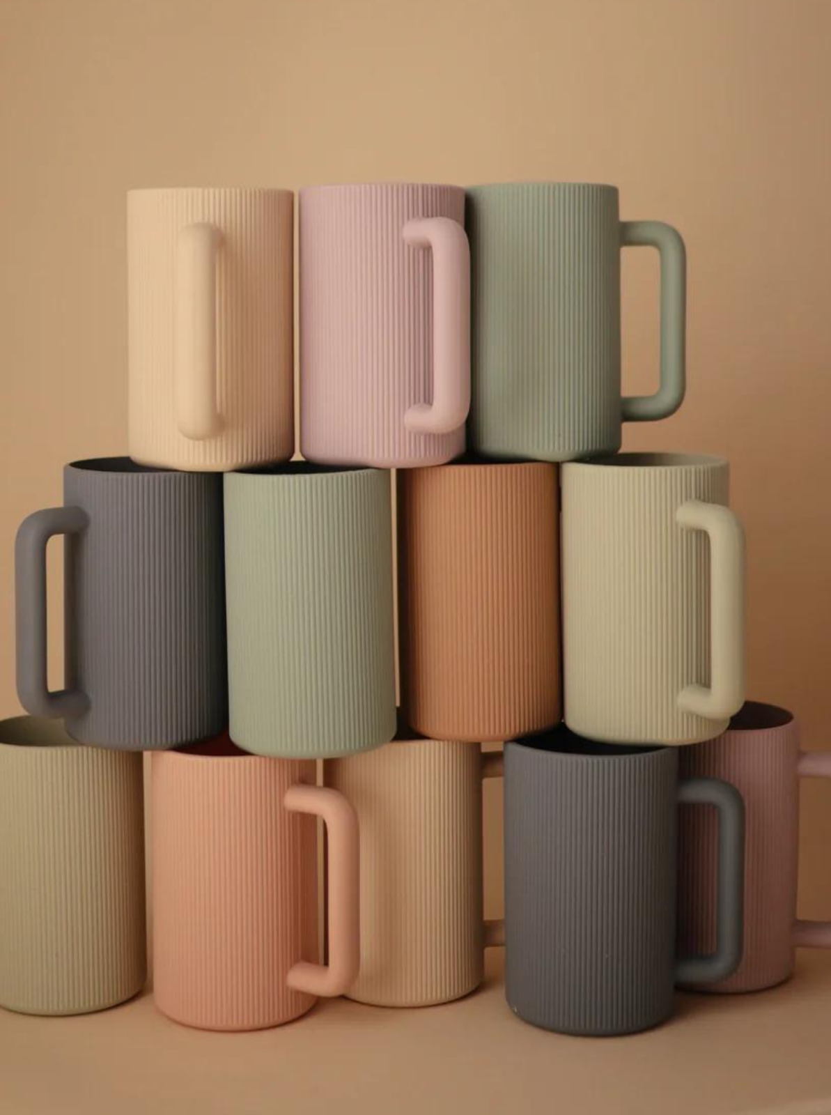 Stack of textured, colorful mugs arranged in a pyramid against a beige background.