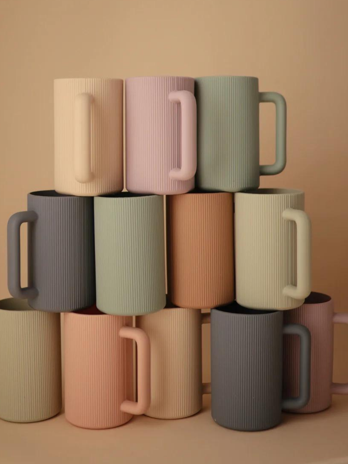 Stack of textured, colorful mugs arranged in a pyramid against a beige background.