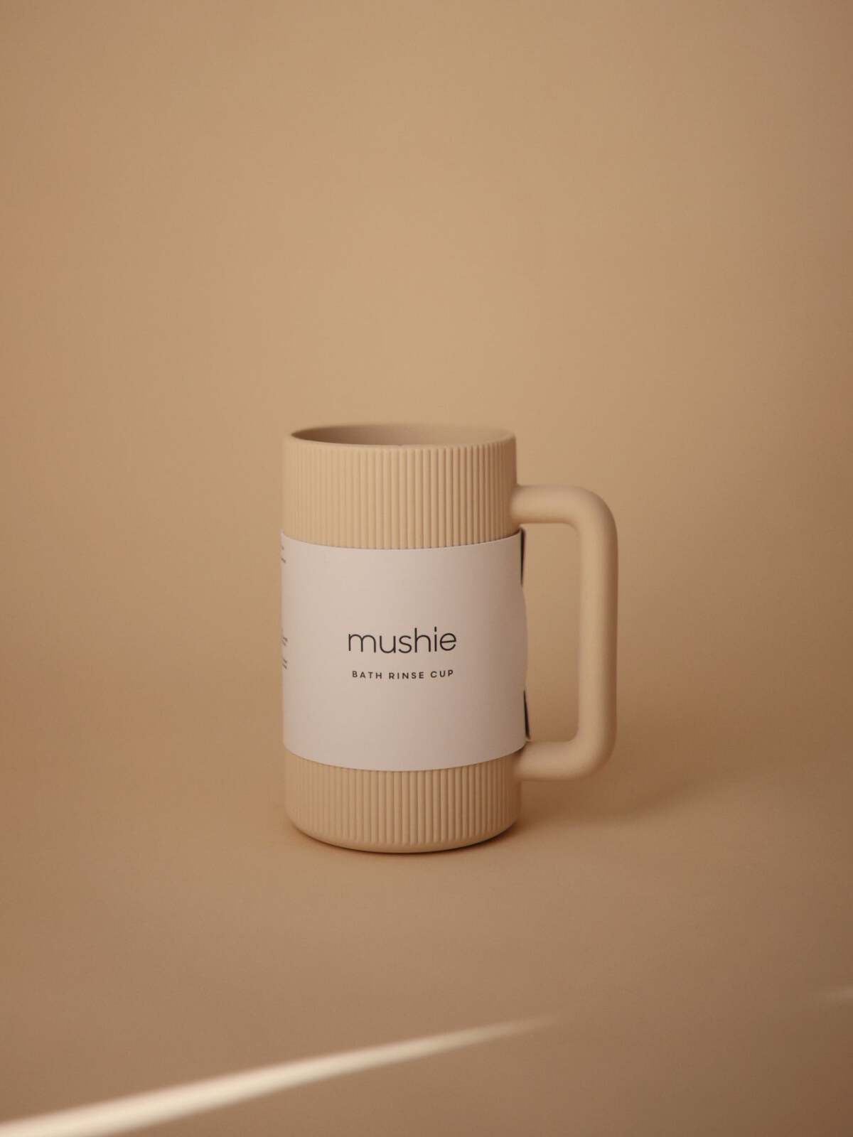 Beige bath rinse cup with ribbed texture and label, placed on a soft brown background.