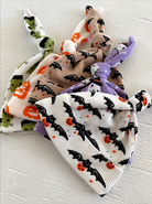 Three Halloween-themed baby hats with bat, pumpkin, and monster designs, tied at the top.