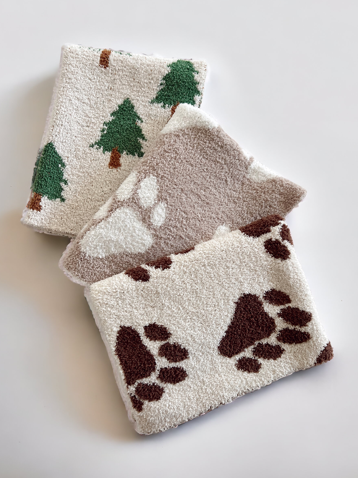 Three textured towels: one with green trees, one with white paws, and one with brown paw prints on a light background.