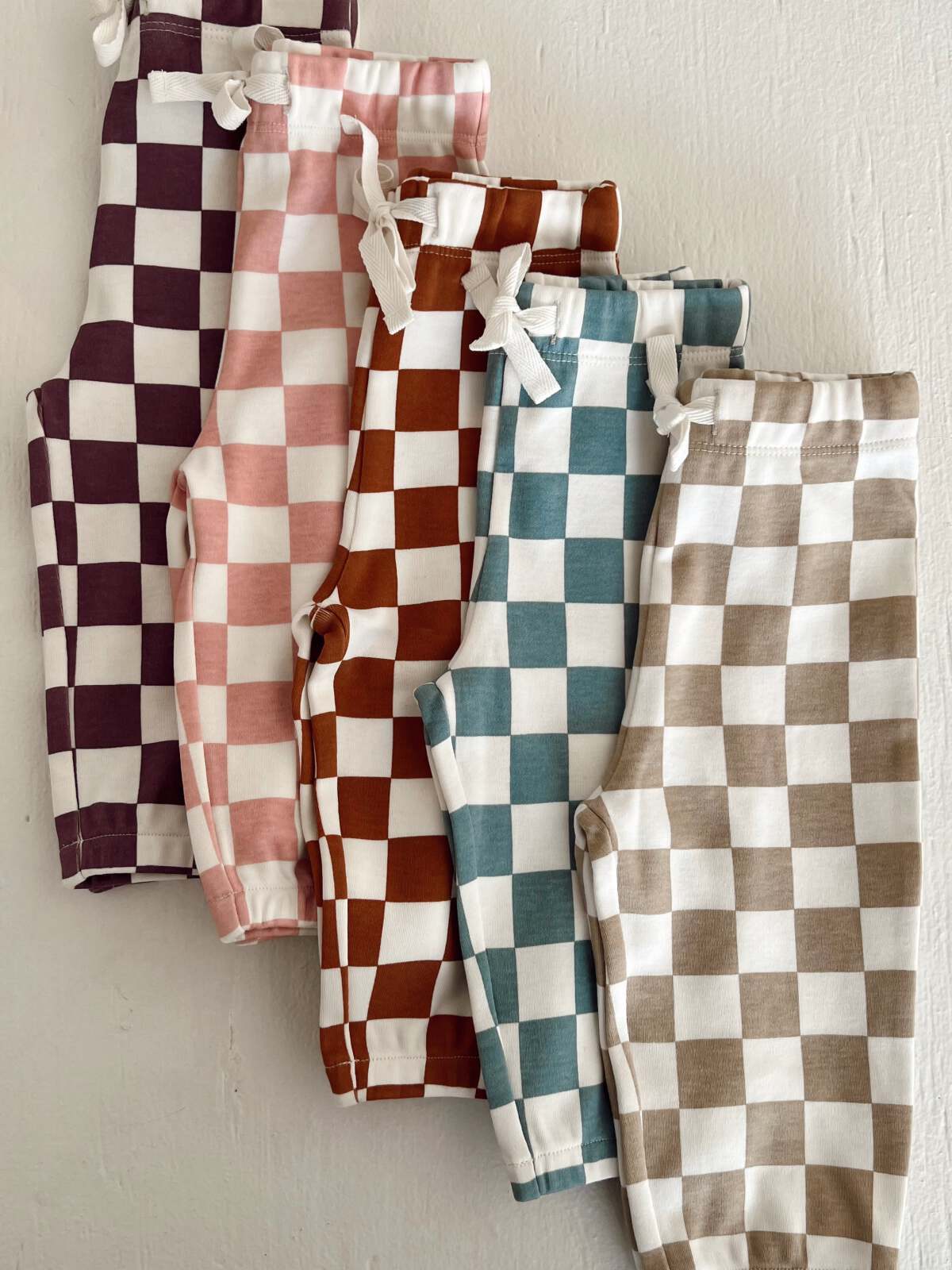Five pairs of checkered pants in various colors: purple, pink, brown, teal, and beige, displayed on a light background.