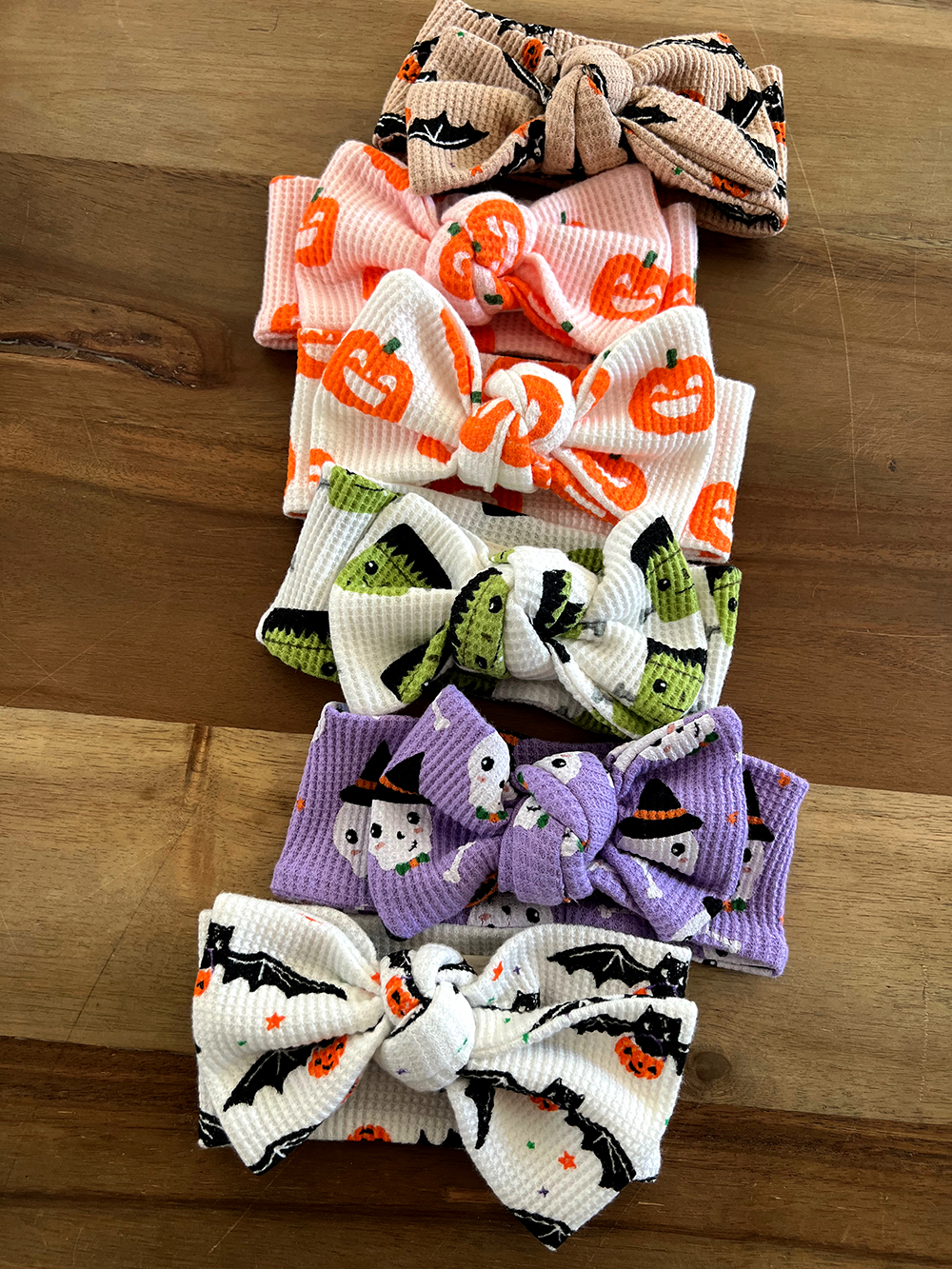 Colorful Halloween-themed hair bows stacked on a wooden surface, featuring pumpkins, ghosts, and bats.