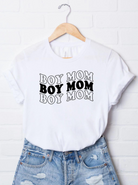 White t-shirt displaying the text "BOY MOM" in a bold, repeated design, paired with distressed denim shorts.