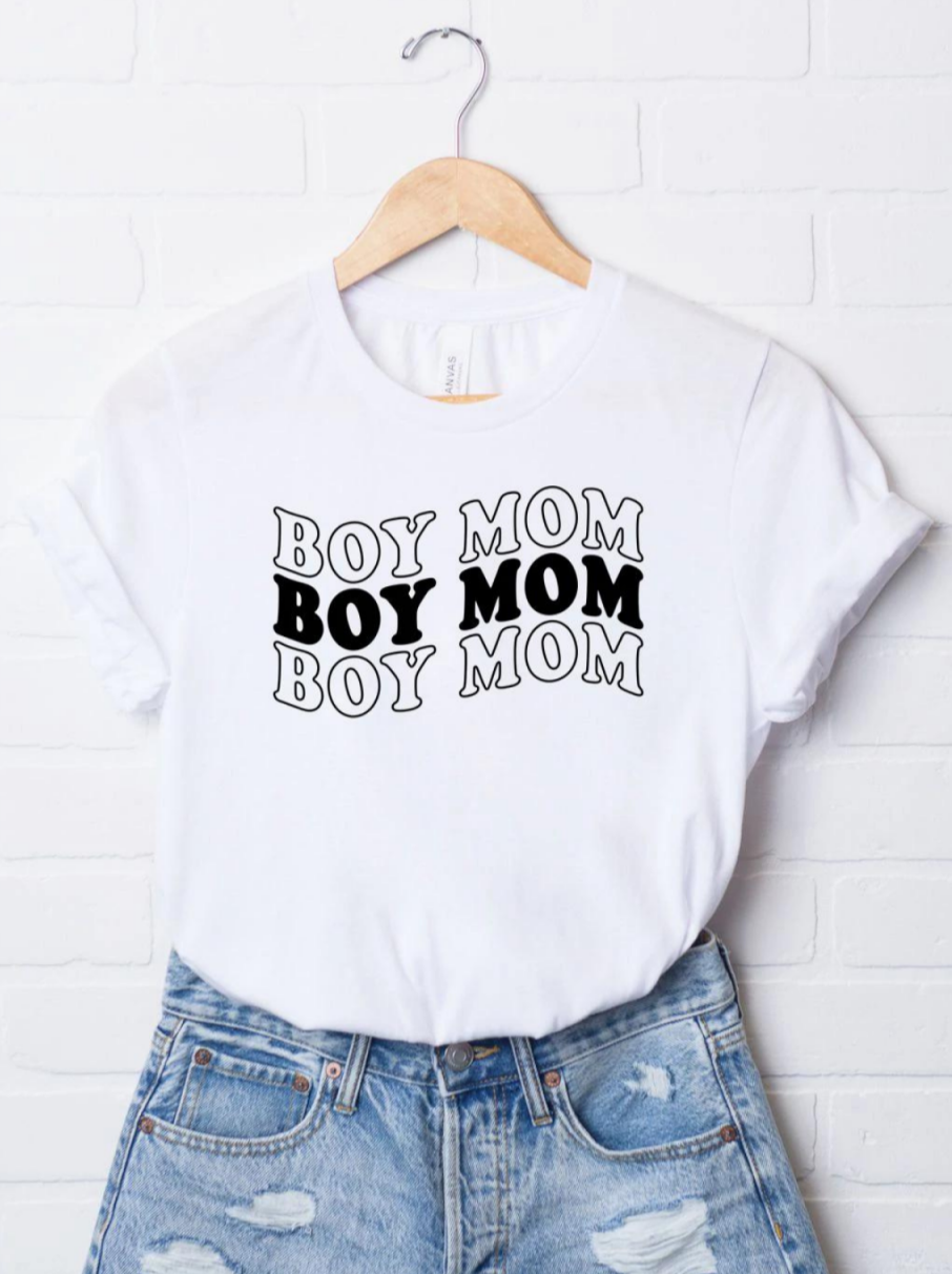 White t-shirt displaying the text "BOY MOM" in a bold, repeated design, paired with distressed denim shorts.