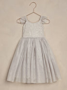 Light gray dress with lace detailing and ruffled sleeves, hanging on a rose gold hanger against a textured background.