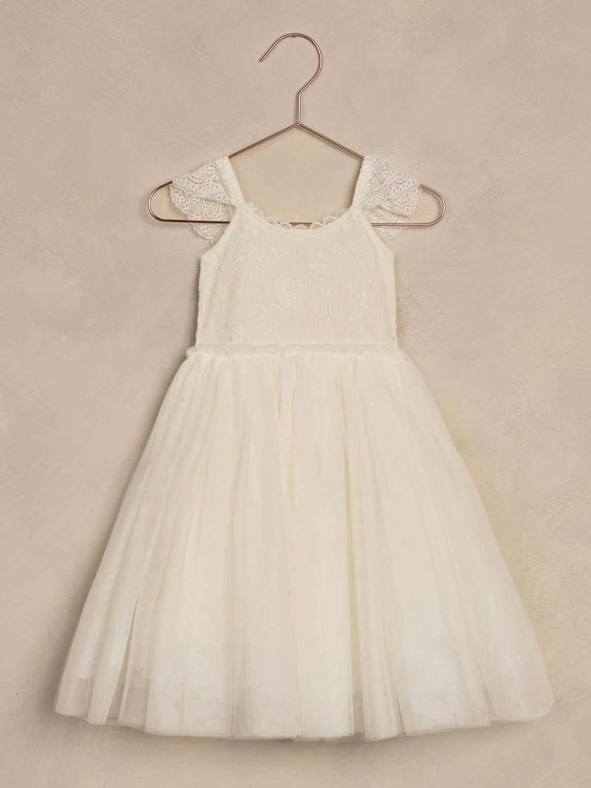 White lace and tulle dress hanging on a copper hanger against a textured background. Perfect for special occasions.
