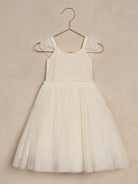 White lace and tulle dress hanging on a copper hanger against a textured background. Perfect for special occasions.
