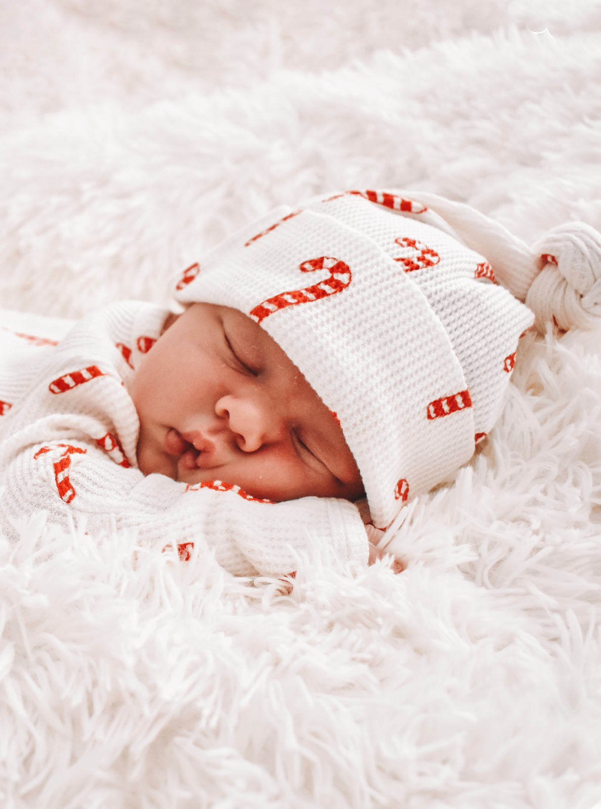 Newborn baby sleeping on a soft blanket, wearing a cozy outfit with candy cane patterns.