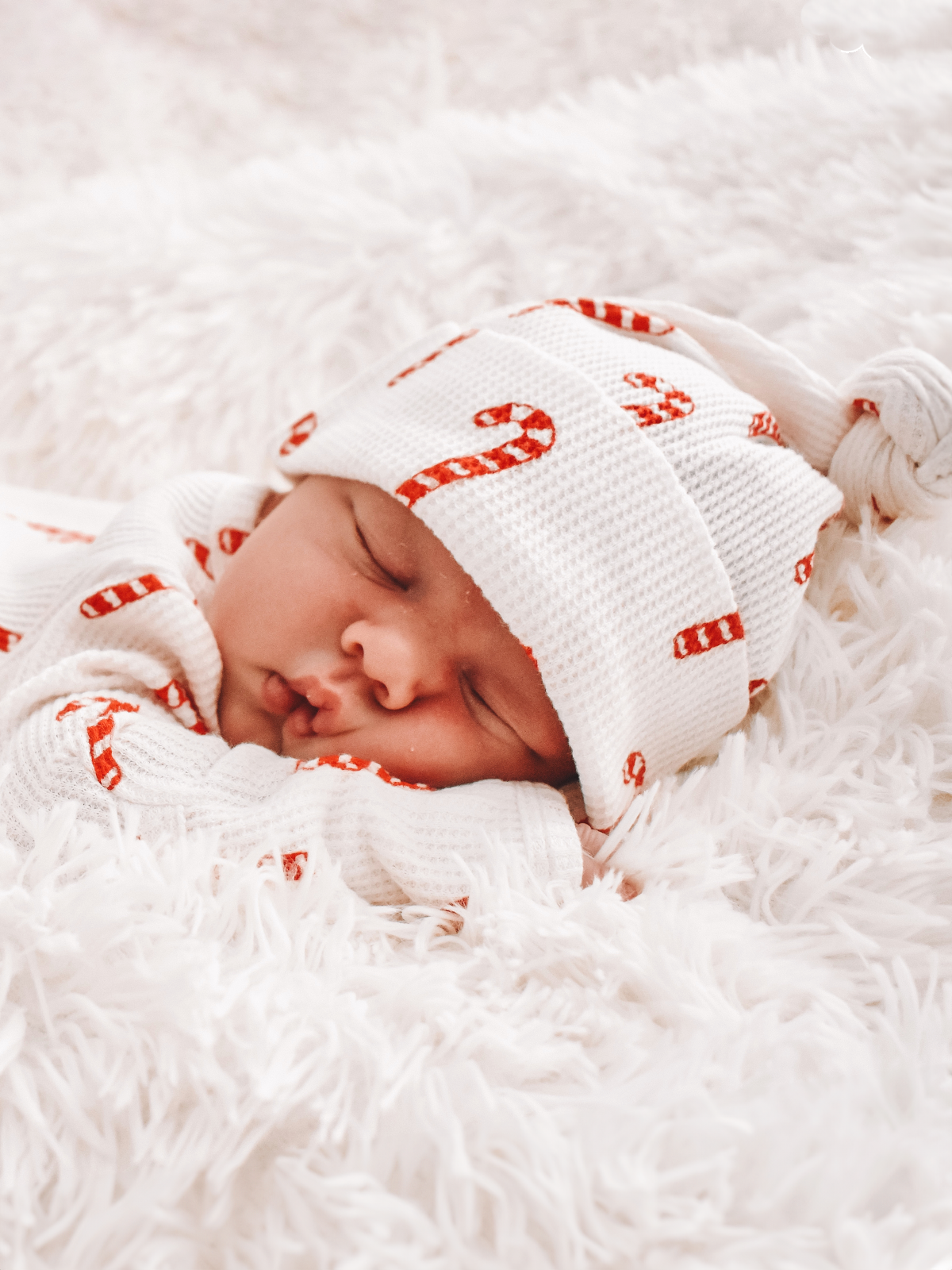 Newborn baby sleeping on a soft blanket, wearing a cozy outfit with candy cane patterns.