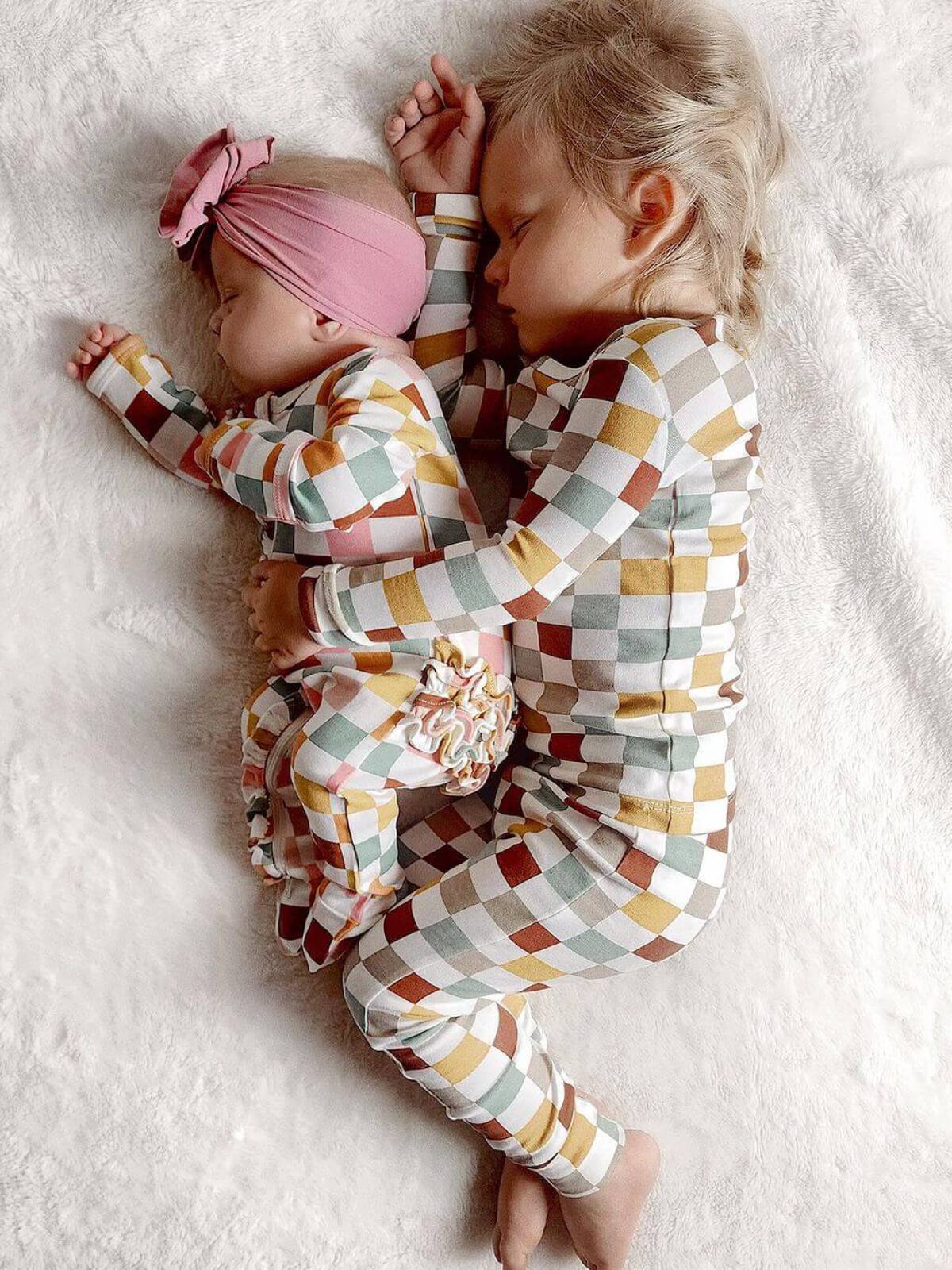Two young children sleeping together on a soft blanket, wearing matching colorful checkered pajamas.