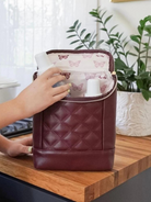 Hand reaching into a burgundy bag with butterfly-patterned lining, set on a wooden table with greenery in the background.