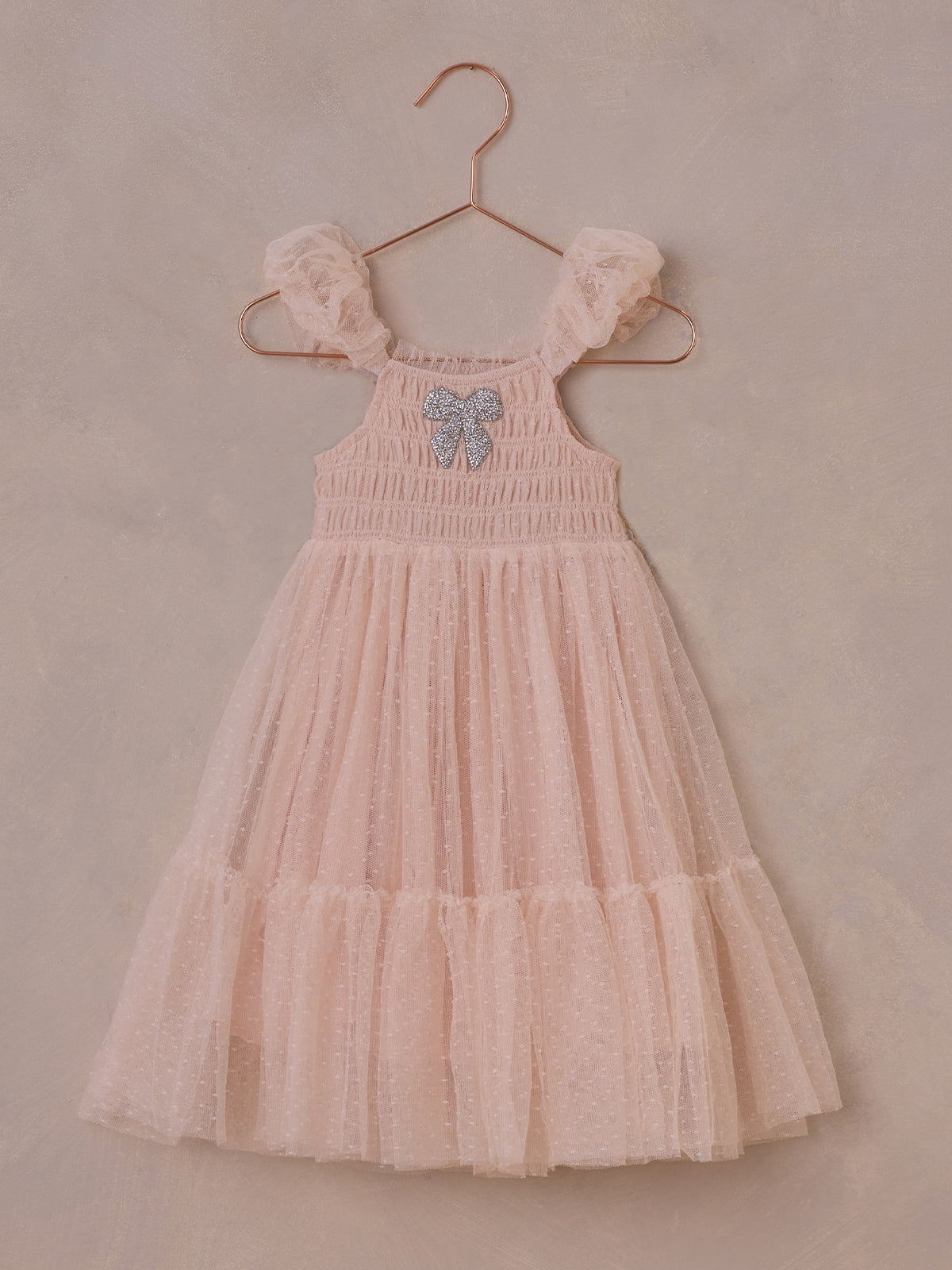 Pink tulle dress with ruffled sleeves and sparkly bow, hanging on a copper hanger against a neutral background.