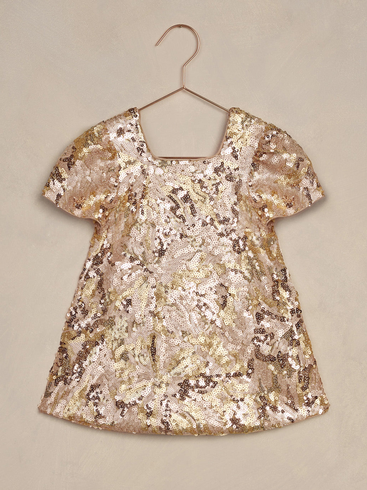 Shiny, sequined gold and pink dress hanging on a hook against a neutral background.