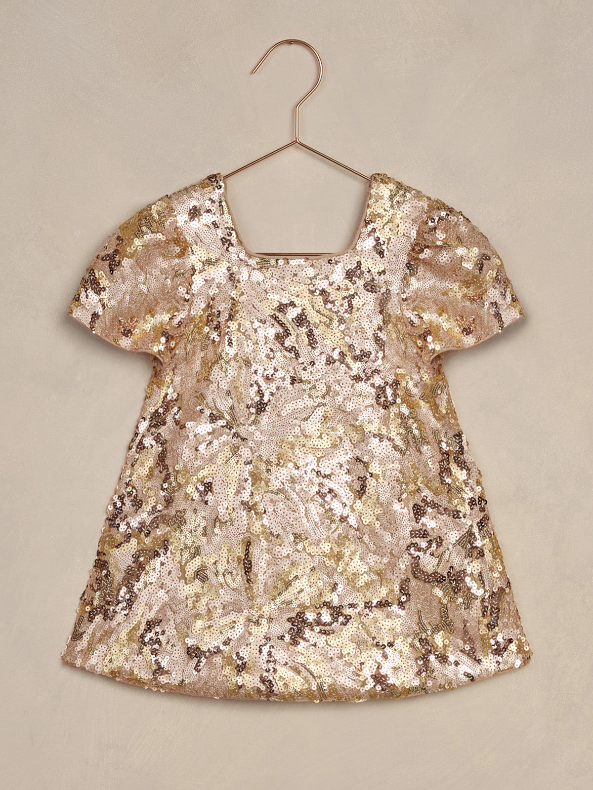 Shiny, sequined gold and pink dress hanging on a hook against a neutral background.