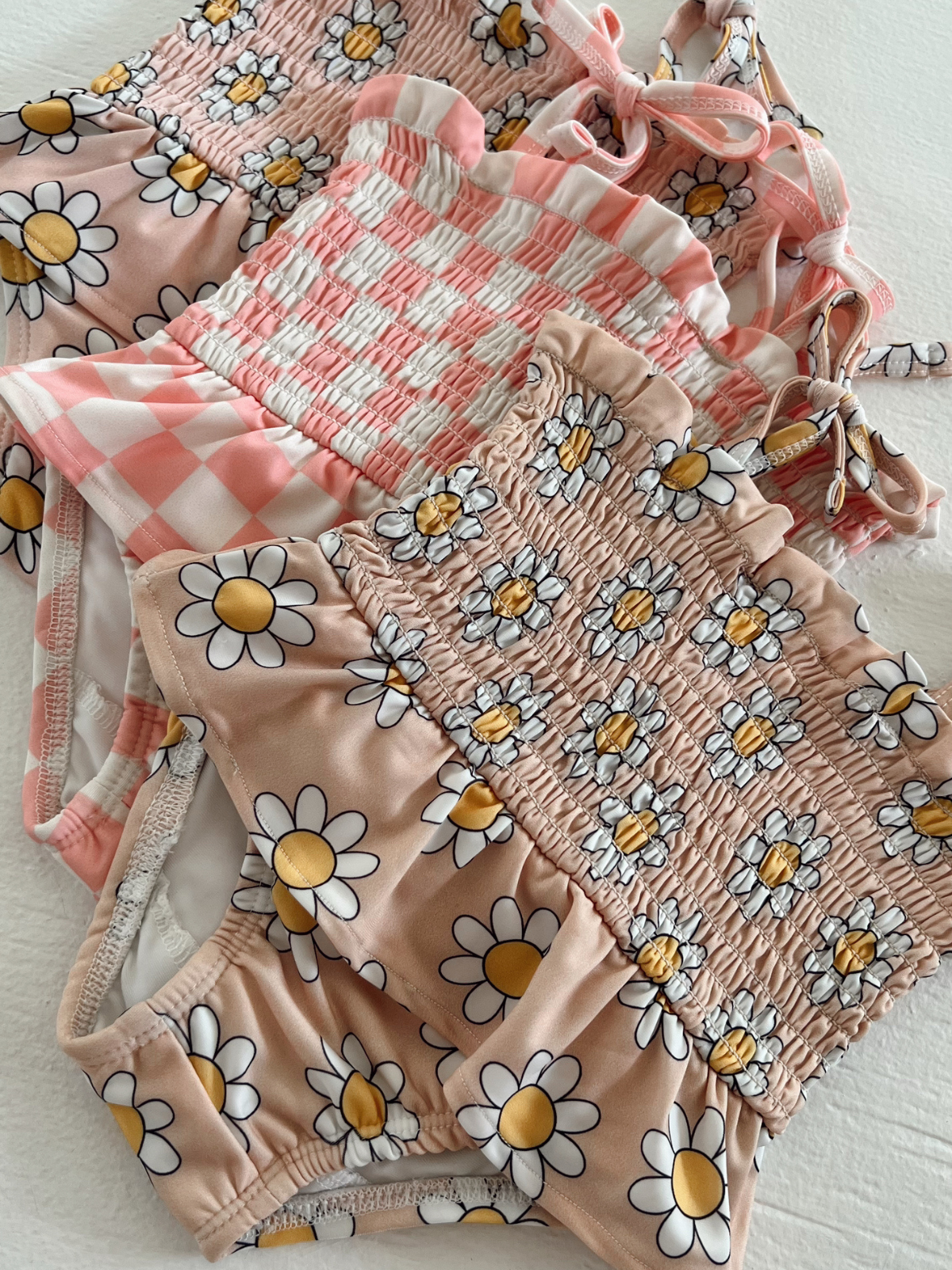 Colorful assortment of floral-patterned swimsuits featuring daisies and gingham designs on a light background.