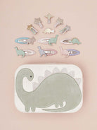 Dinosaur-themed hair clips arranged around a dinosaur-shaped storage case on a light background.