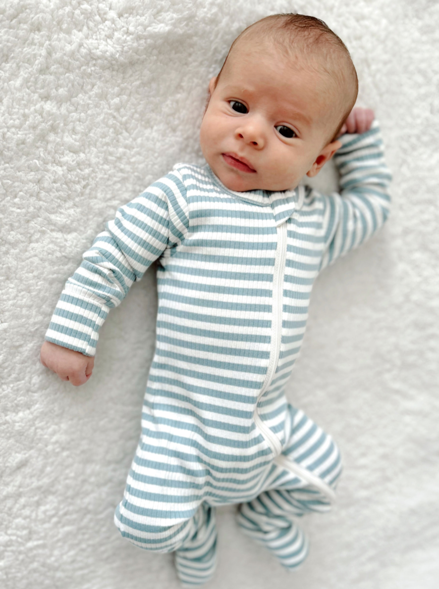 Infant lying on a soft blanket, wearing a blue and white striped onesie, with a curious expression.