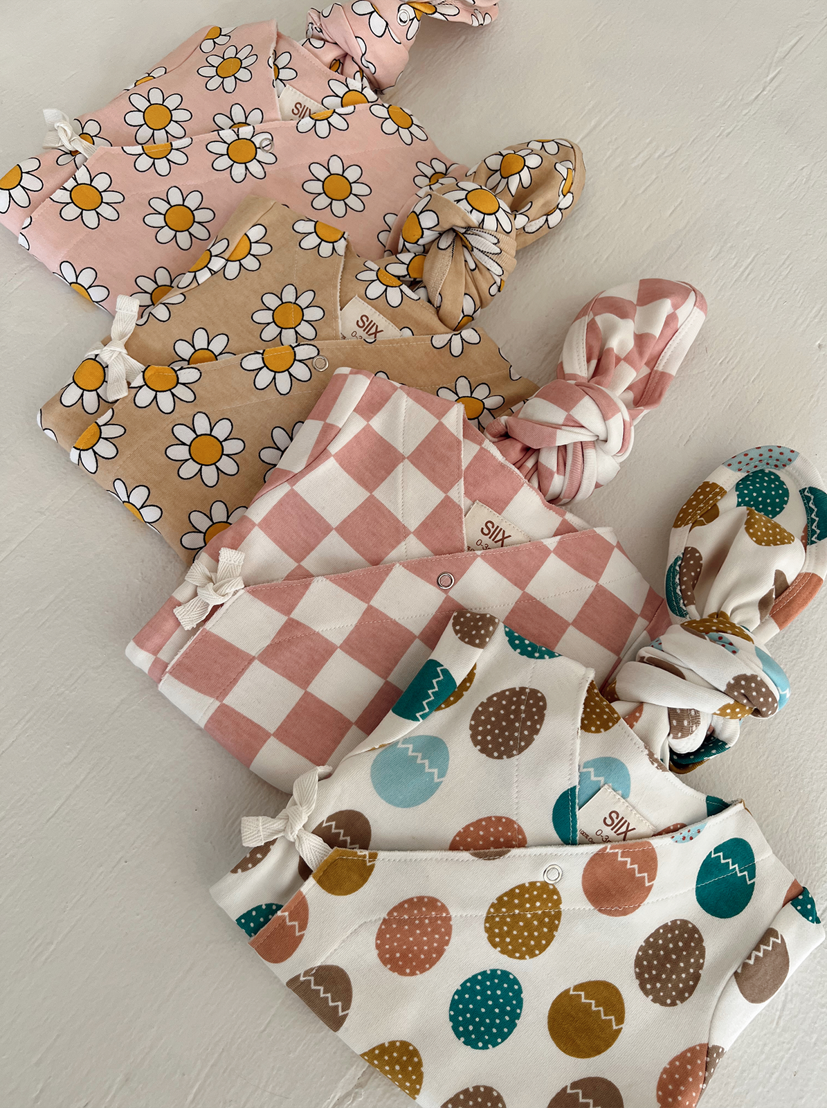 Two sets of patterned baby blankets and hats in floral and geometric designs on a light background.