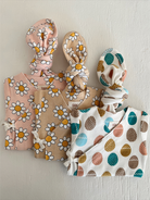 Three baby outfits with floral and egg patterns on a neutral background. Ideal for spring fashion.