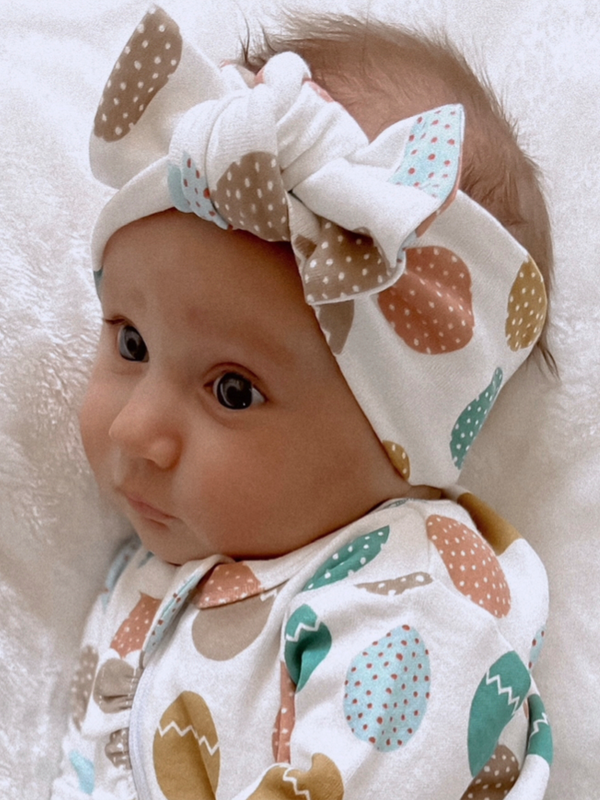 Baby with a stylish polka dot headband and colorful onesie, lying on a soft blanket.
