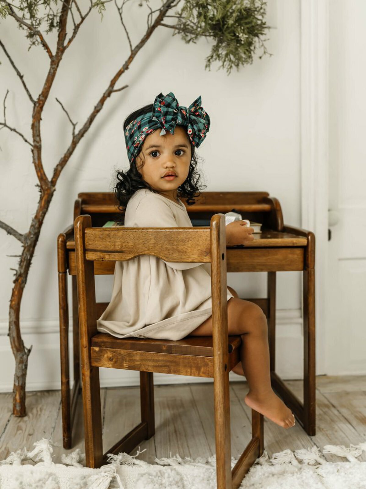 Young child with curly hair and a patterned headband sitting at a wooden table, looking back over their shoulder.