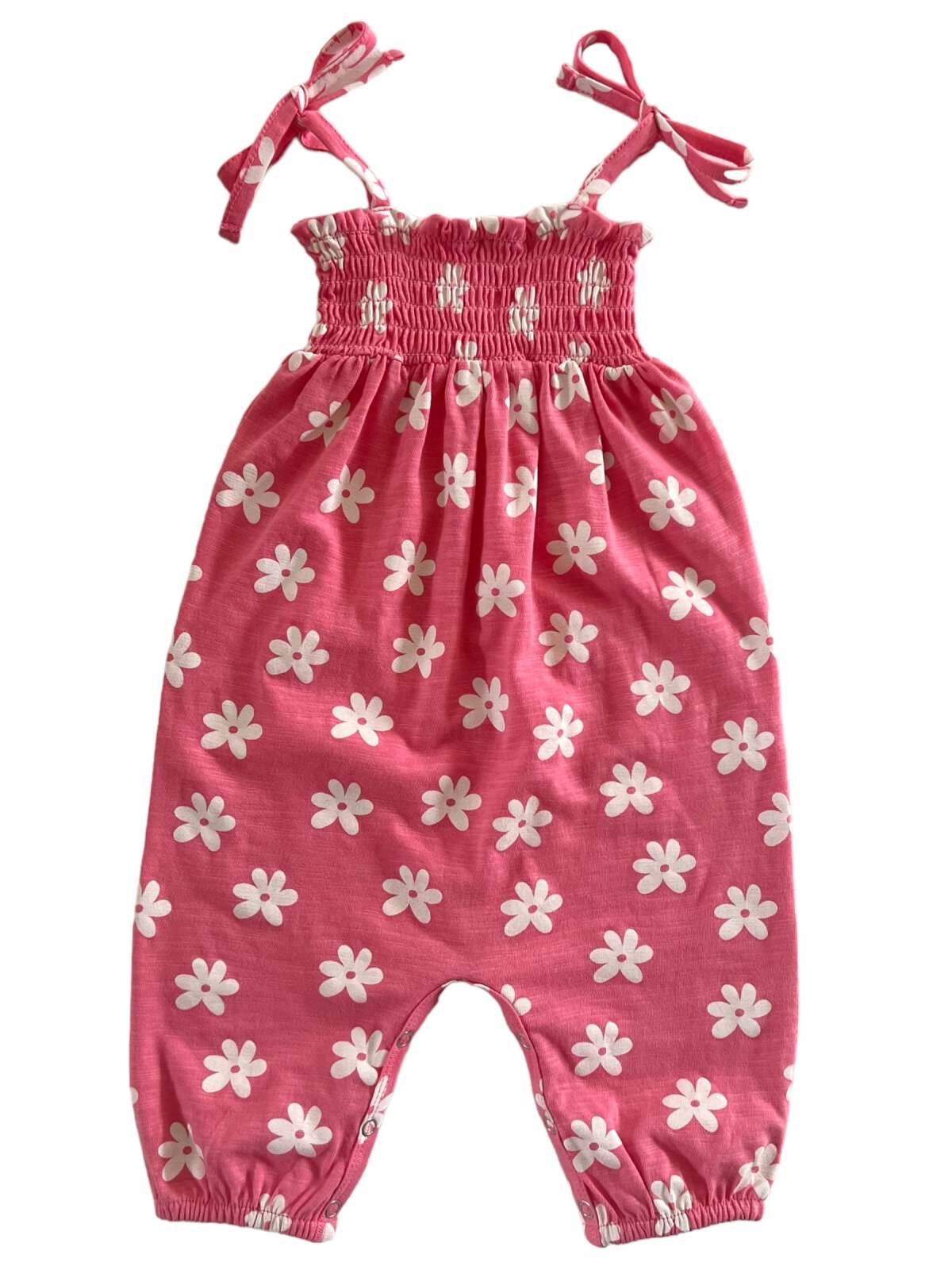 Pink baby romper with white floral print and tie straps, featuring smocked bodice and elastic cuffs.