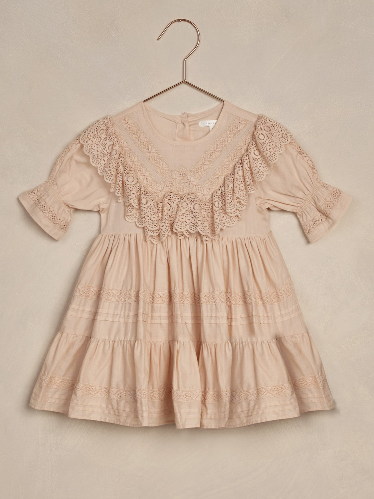 Light pink dress with lace detailing, hung on a copper hanger against a pale background.