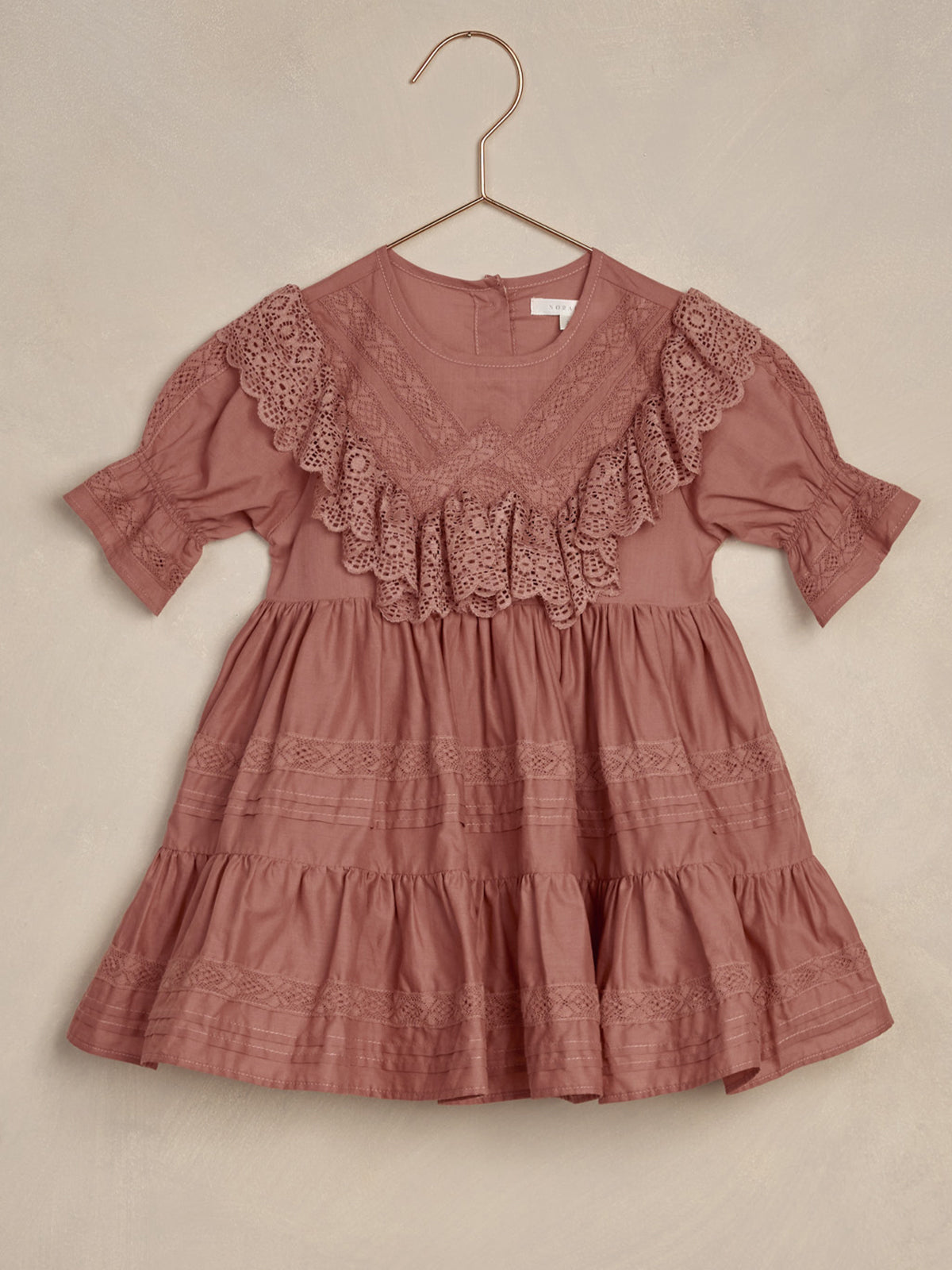 Pink ruffled dress with lace trim, hanging on a hook against a neutral background.