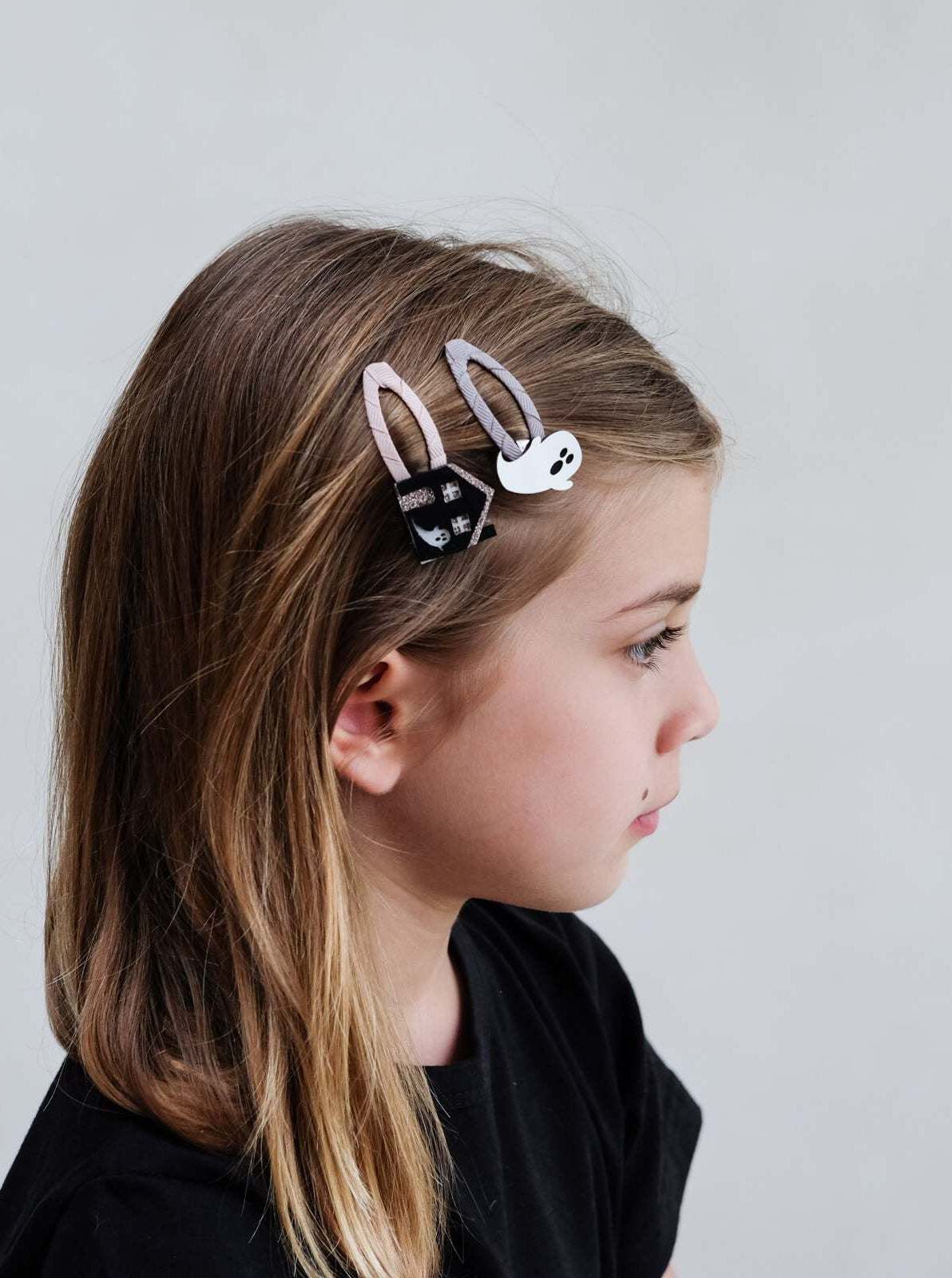 Girl with long hair wearing bunny-shaped hair clips, side profile against a light gray background.