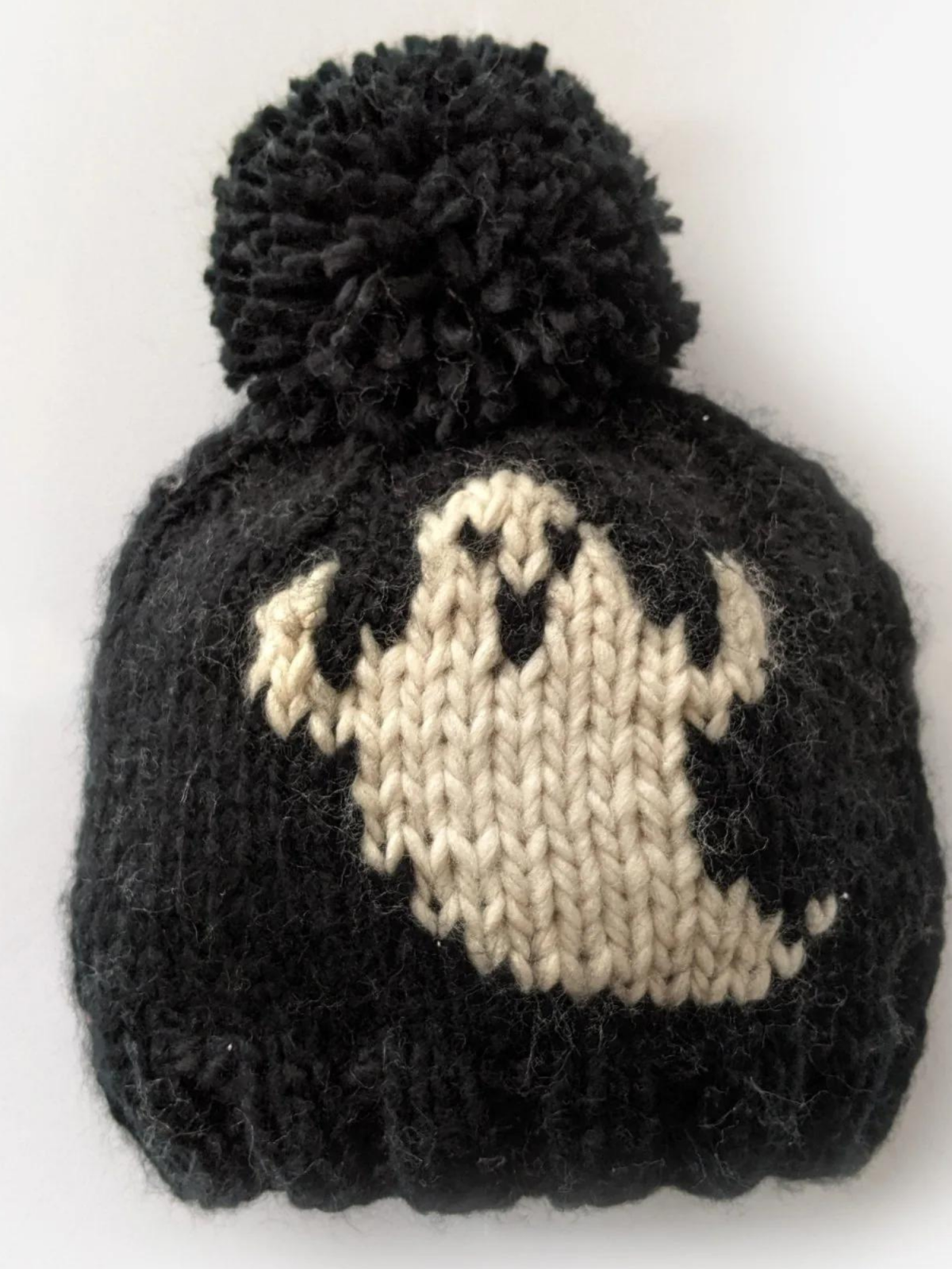 Black knit beanie with a white ghost design and a fluffy pom-pom on top.