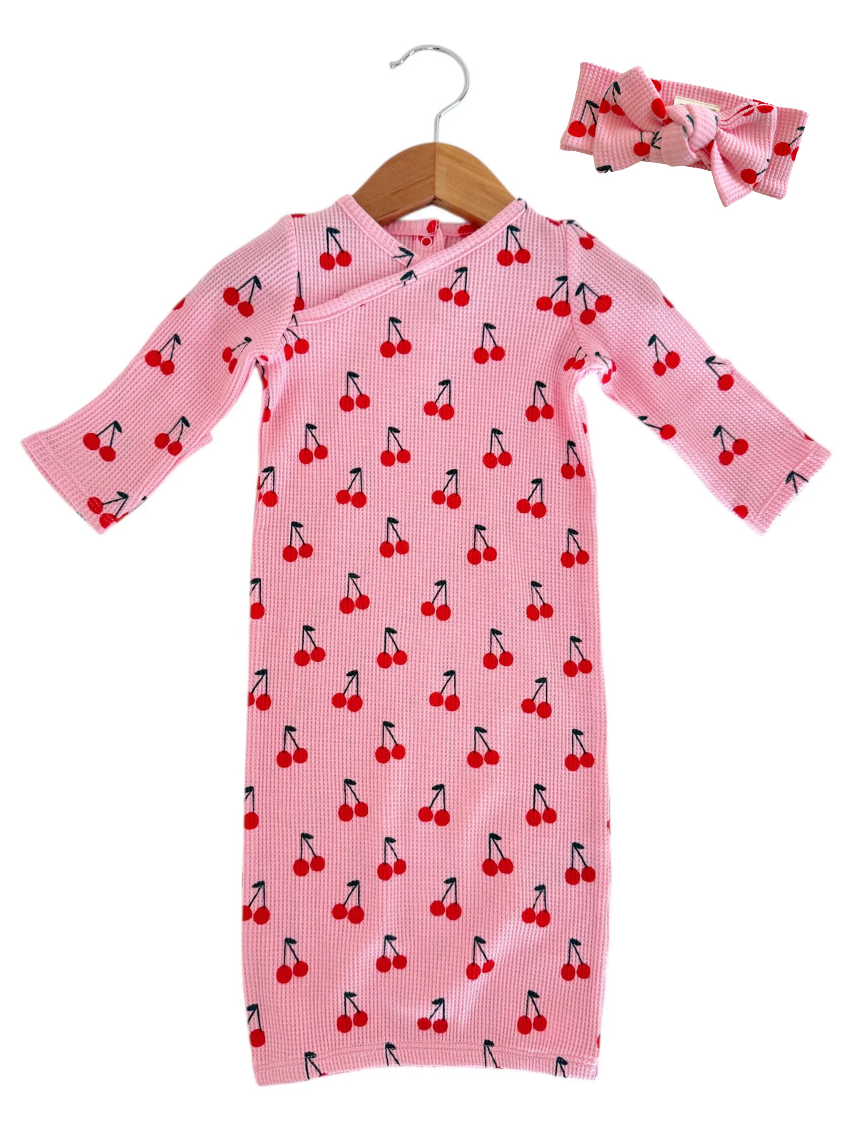 Pink baby dress with cherry pattern and matching headband, hanging on a wooden hanger.