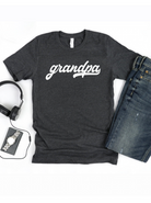 Gray t-shirt with "grandpa" printed in white, paired with jeans, headphones, watch, and wallet.