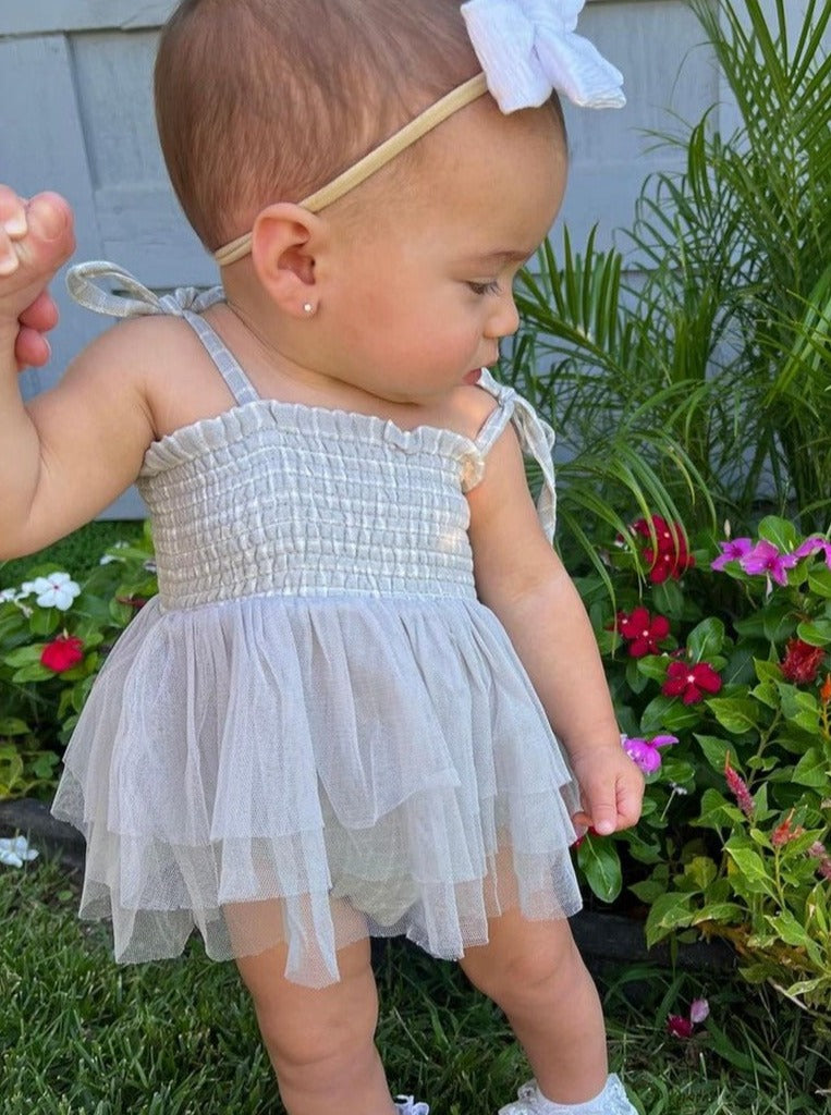 Toddler wearing a light gray dress with tulle layers, standing in a garden with colorful flowers.