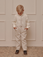 Young boy in stylish outfit, hands in pockets, standing against a textured backdrop.