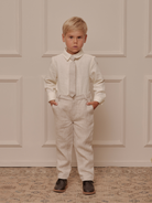 Young boy in light outfit with a tie, standing confidently in front of a textured backdrop.
