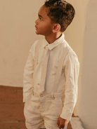 Young boy in a light linen suit and tie, standing against a soft beige background.