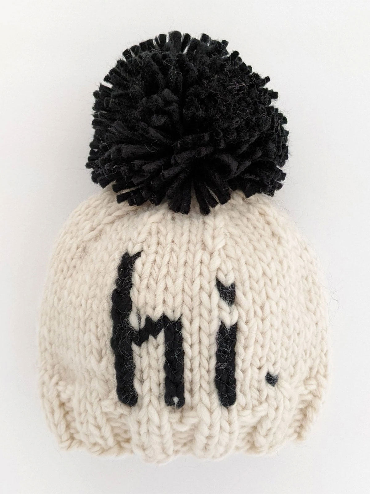 Knit beanie with black pom-pom and the word "hi" in bold black letters on a cream background.