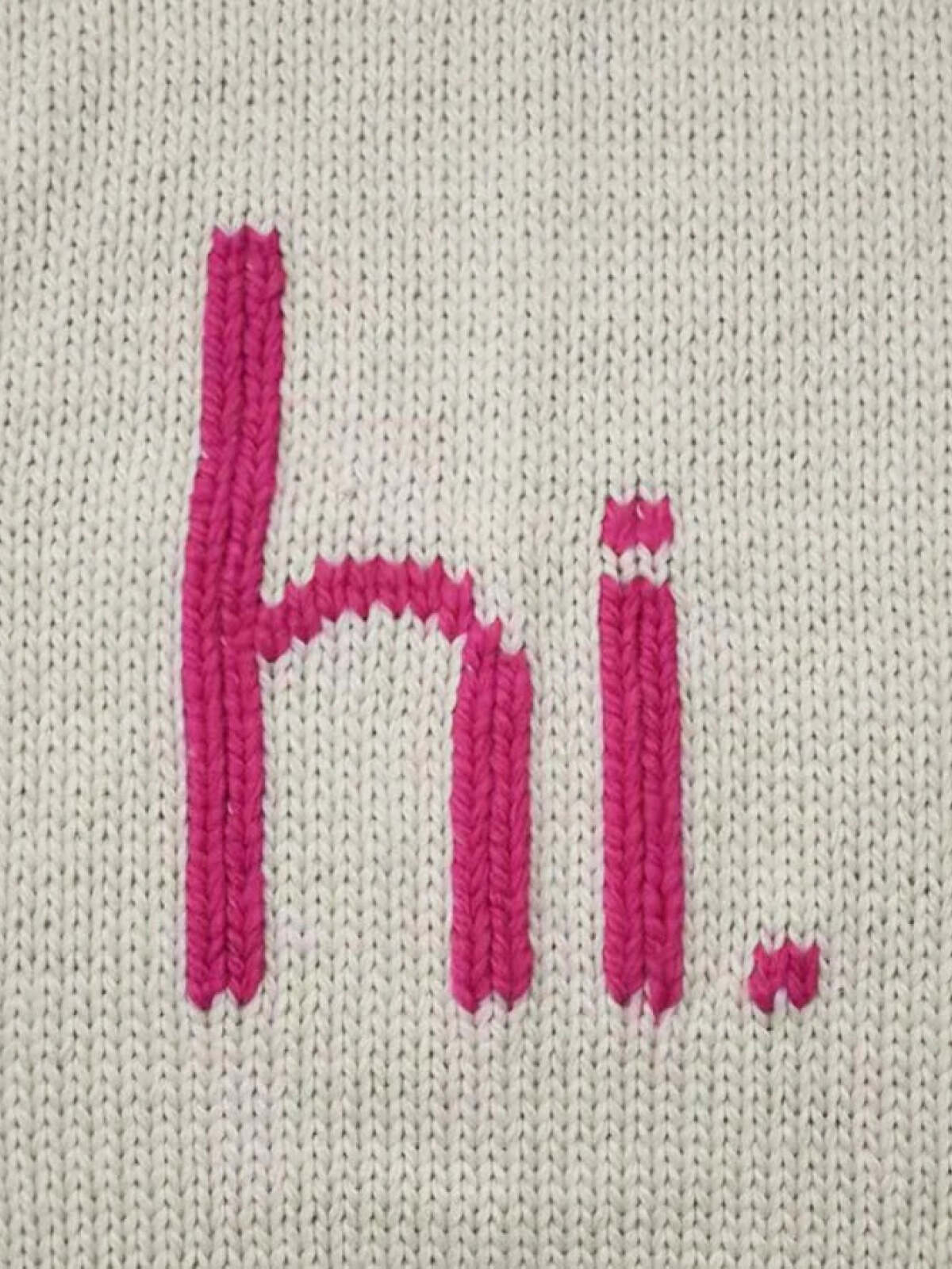 Pink embroidered "hi." on a textured light gray fabric background.