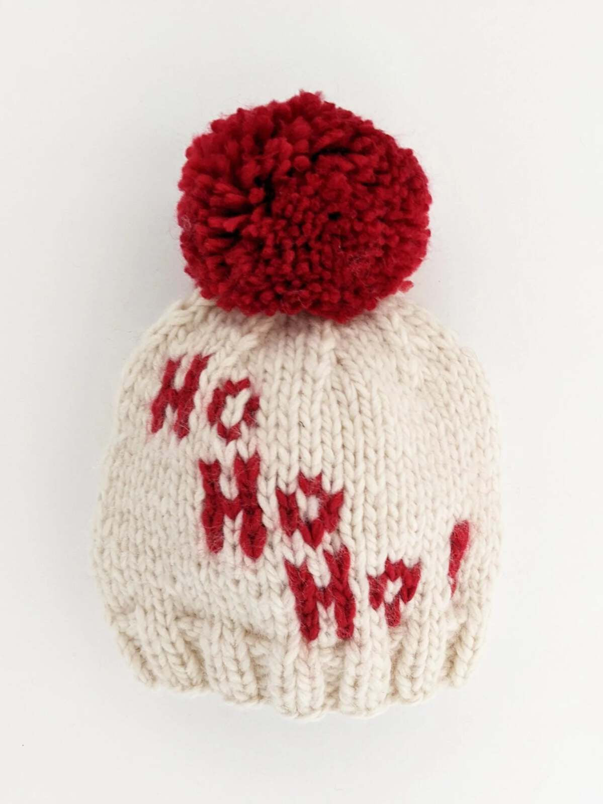 White knit beanie with red lettering "Ho Ho Ho" and a large red pom-pom on top.