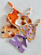 Four colorful baby hats with Halloween patterns: pumpkins, ghosts, and candy corn on a light background.
