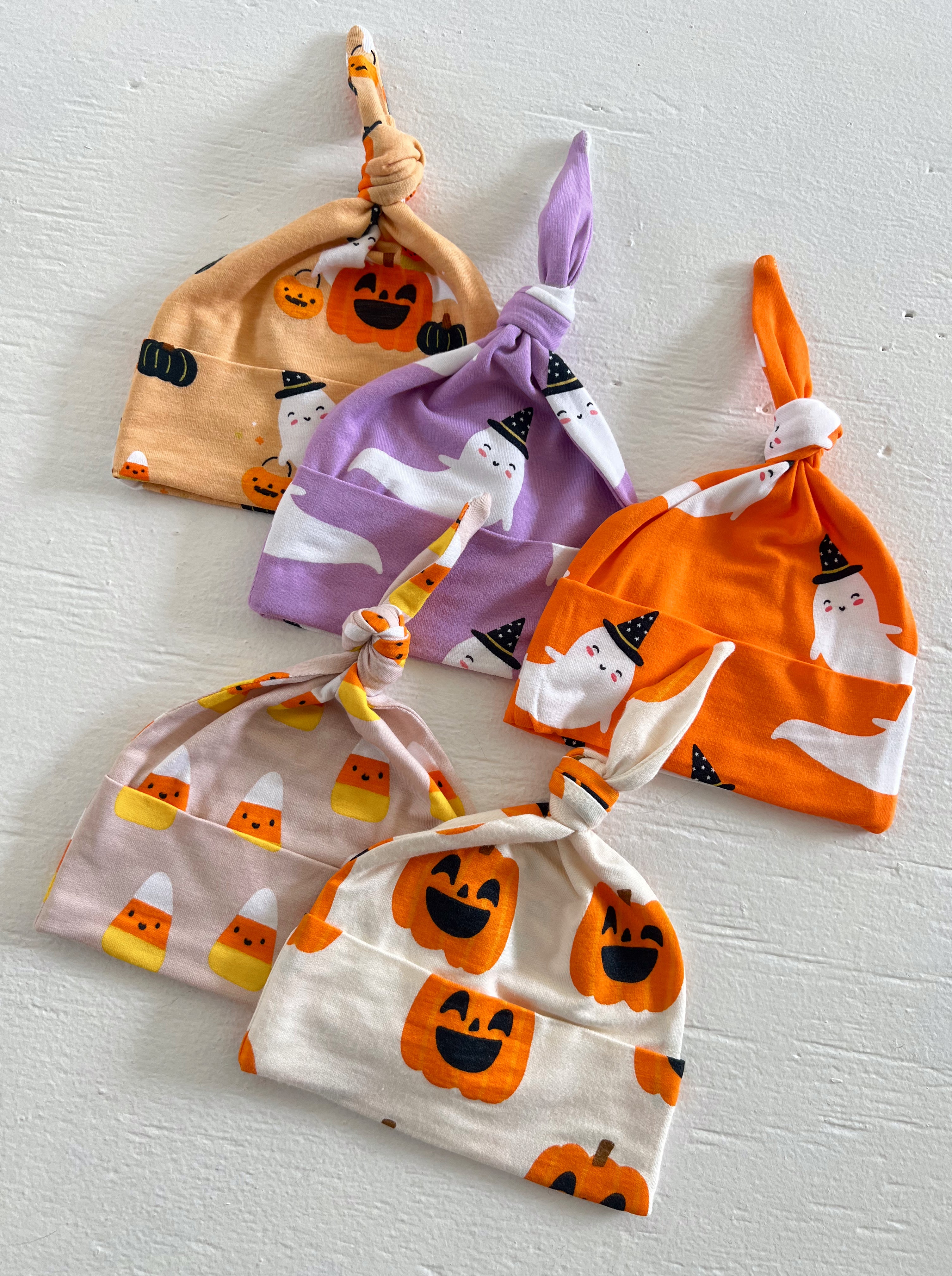 Five colorful baby hats with Halloween designs, including pumpkins, ghosts, and candy corn, arranged neatly.