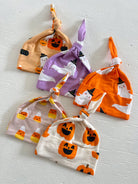 Five colorful baby hats with Halloween designs, including pumpkins, ghosts, and candy corn, arranged neatly.