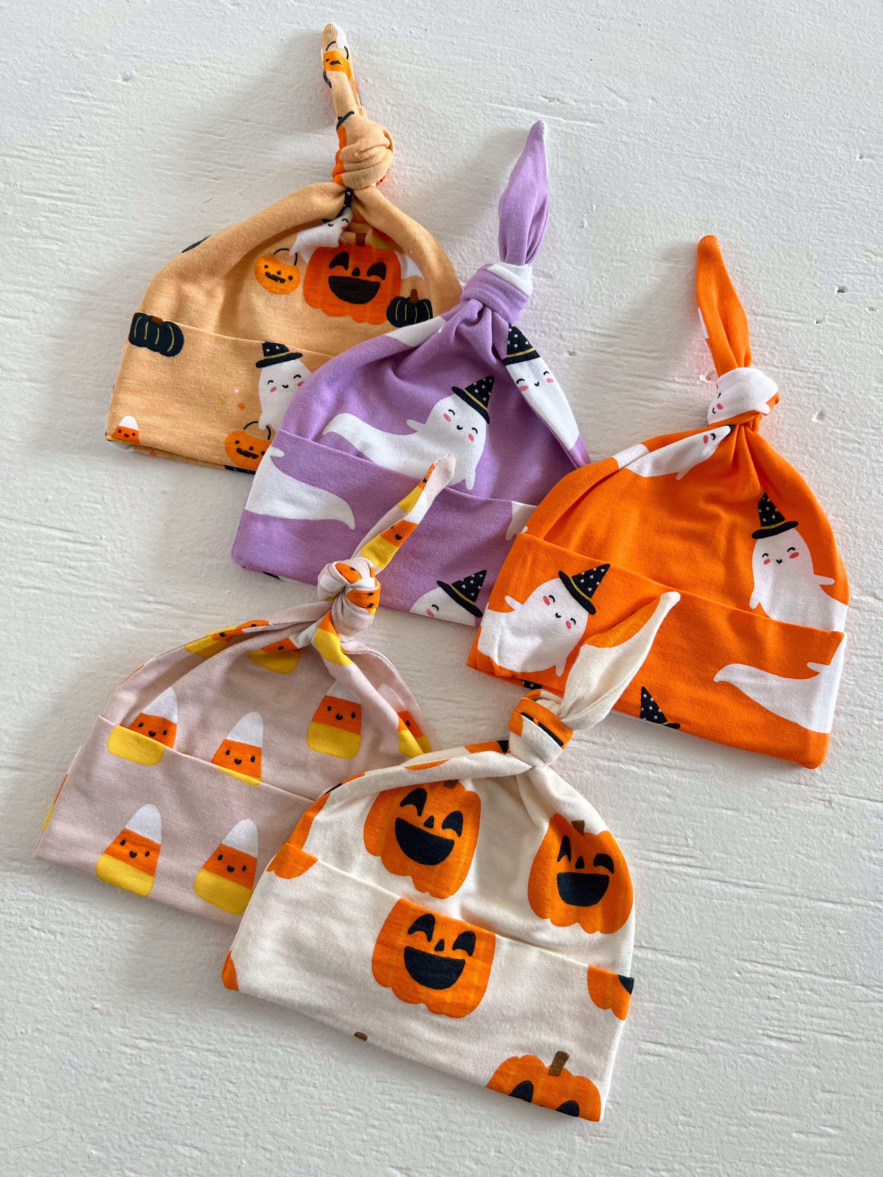 Five colorful baby hats with Halloween designs, including pumpkins, ghosts, and candy corn, arranged neatly.
