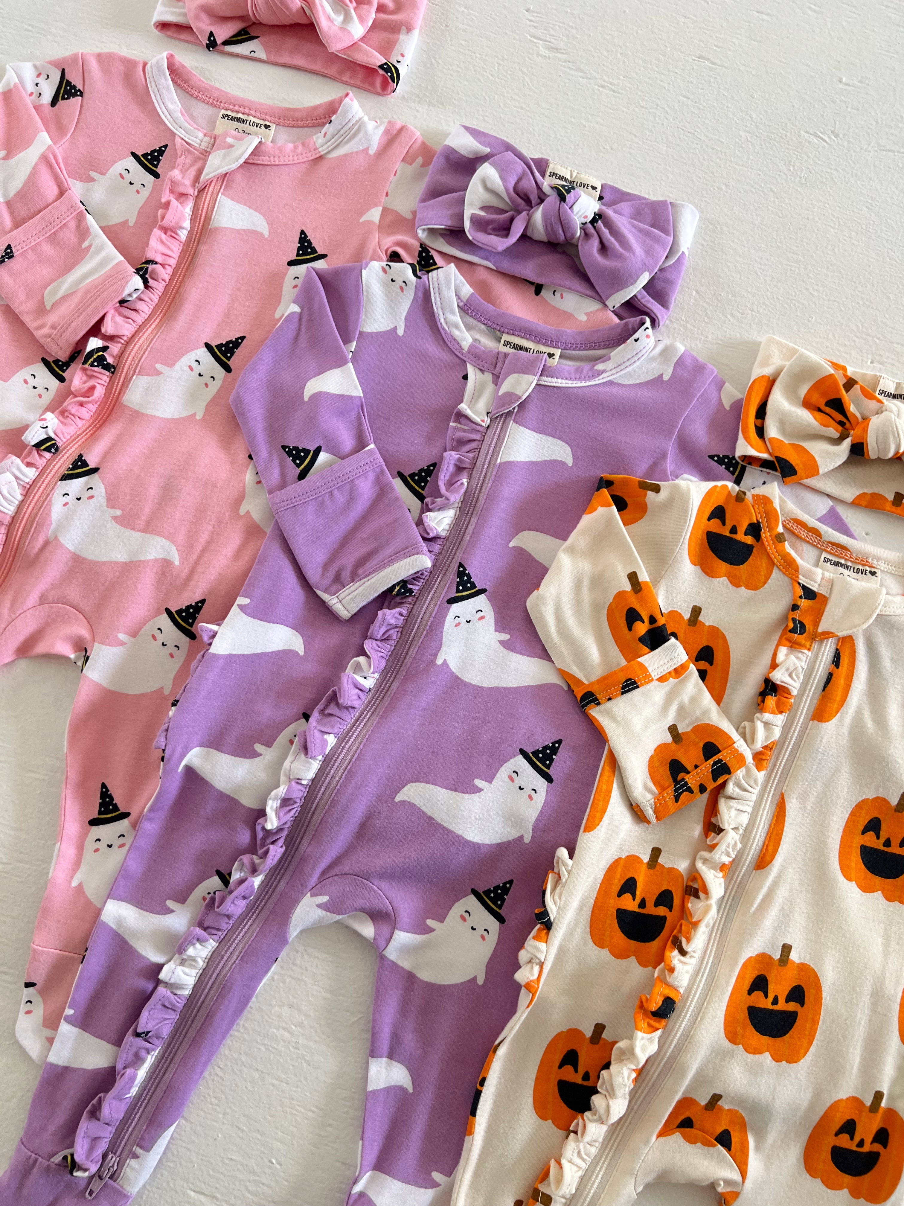 Colorful baby onesies with ghost and pumpkin designs, featuring ruffles and matching headbands. Perfect for Halloween.
