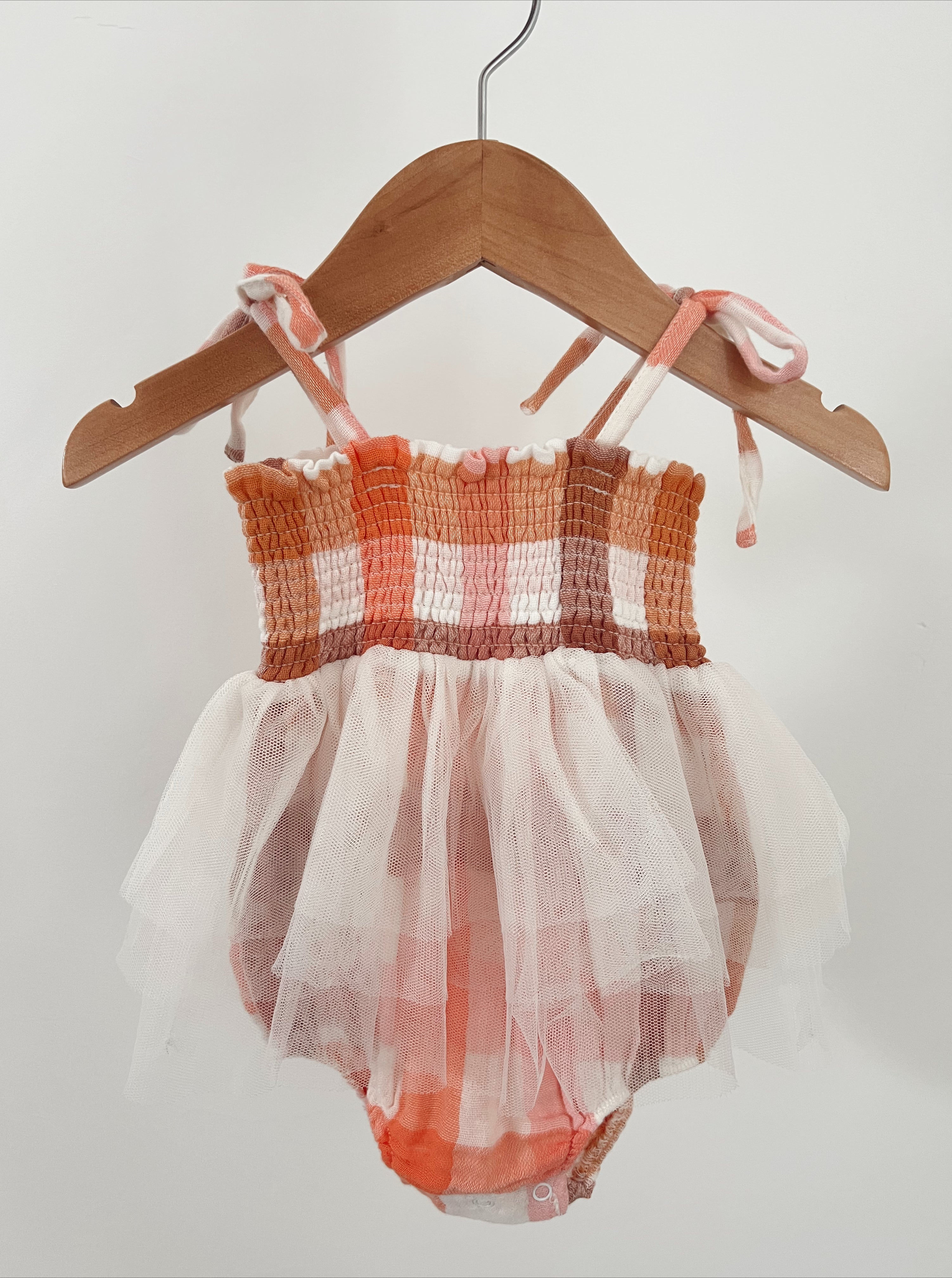 Toddler dress with colorful checked pattern and tulle skirt hanging on a wooden hanger against a light background.