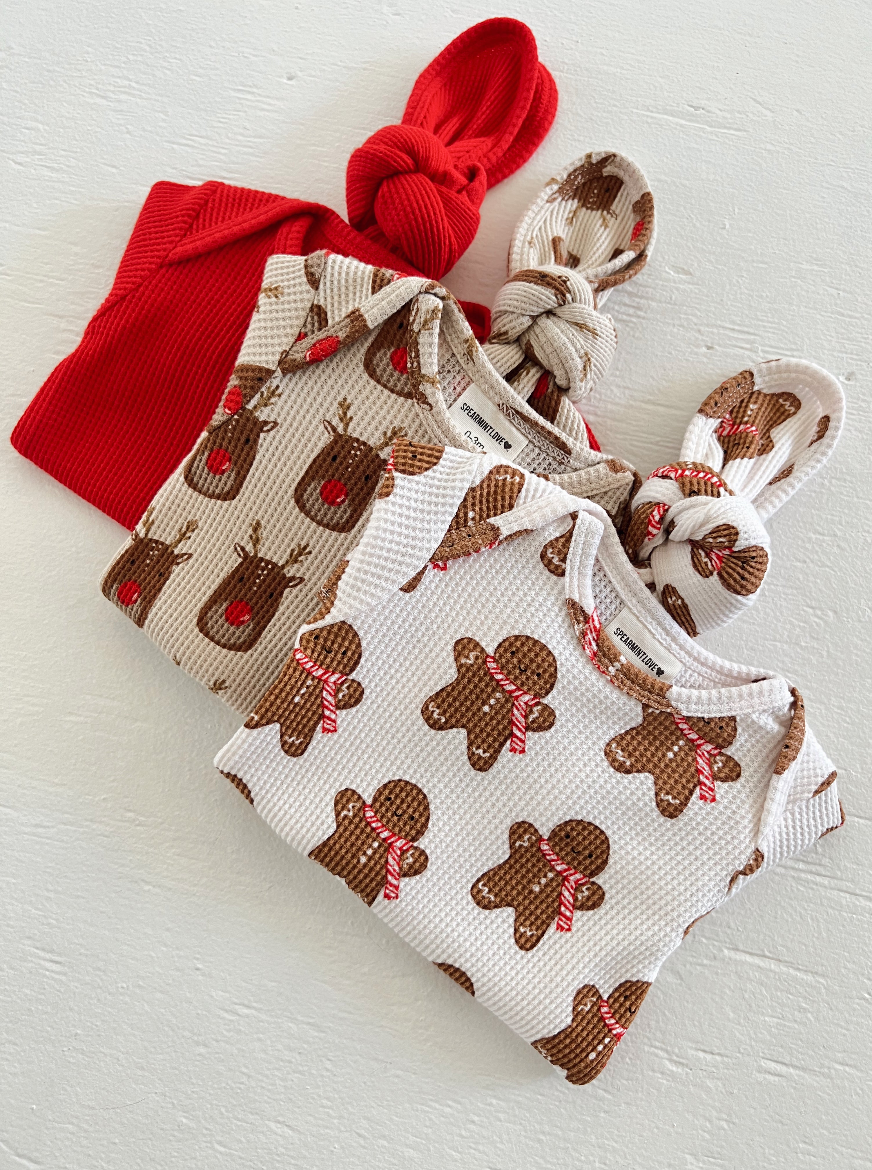 Three baby hats: red and patterned with reindeer and gingerbread men, perfect for festive occasions.